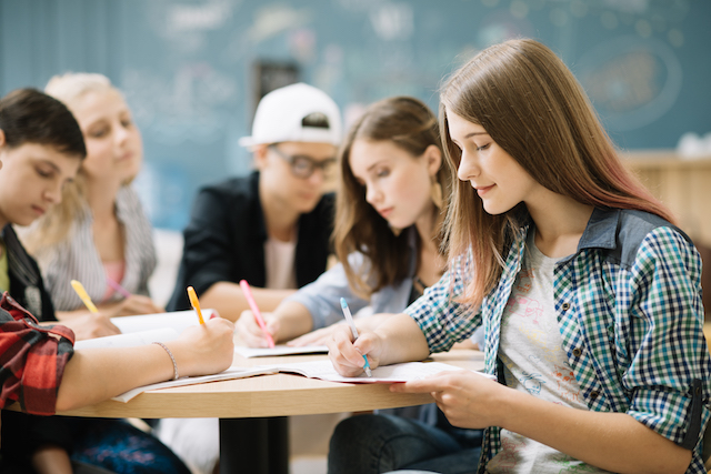 Group of students writing in cursive, looking focused.