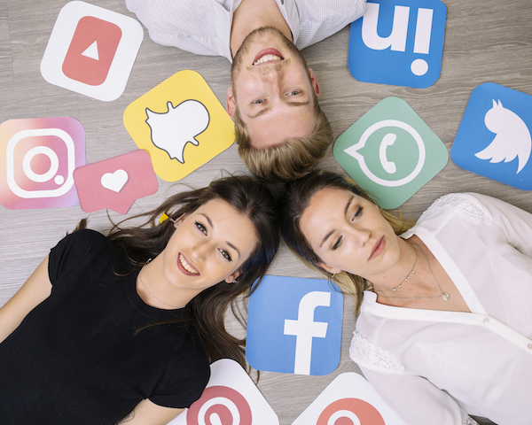 Friends lying on ground, surrounded by social media icons, some happy and some sad.