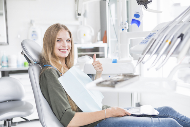 woman at dentist office with a thumb up and smiling.