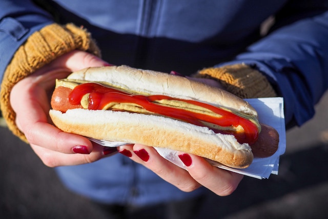 hands holding a hot dog topped with ketchup and mustard.