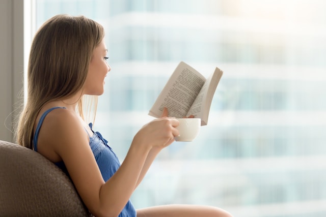 a woman reading, relaxed holding a cup of coffee.