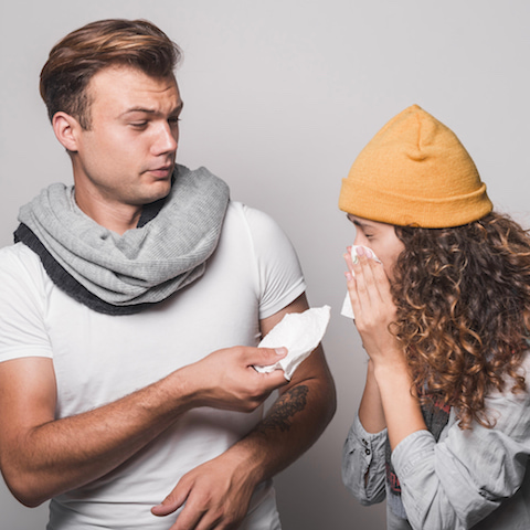 man, grossed out, providing a tissue to a sneezing woman.