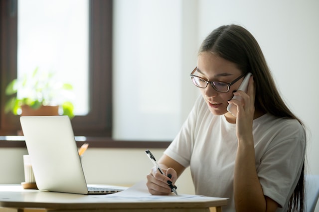 woman at a laptop making a phone reservation, which can have hidden fees.