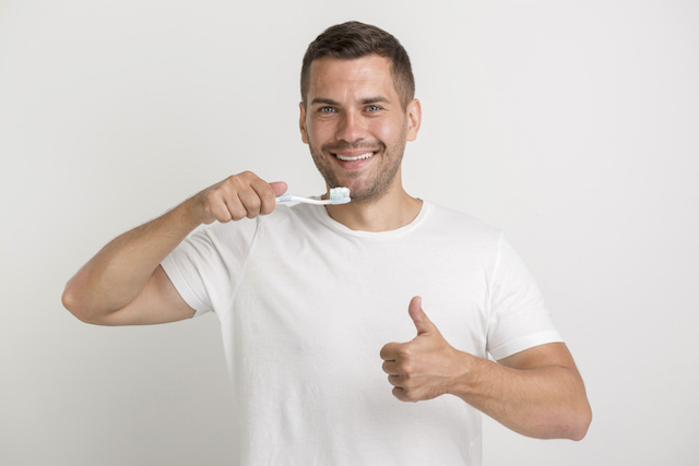 man smiling with thumbs up, brushing his teeth. 