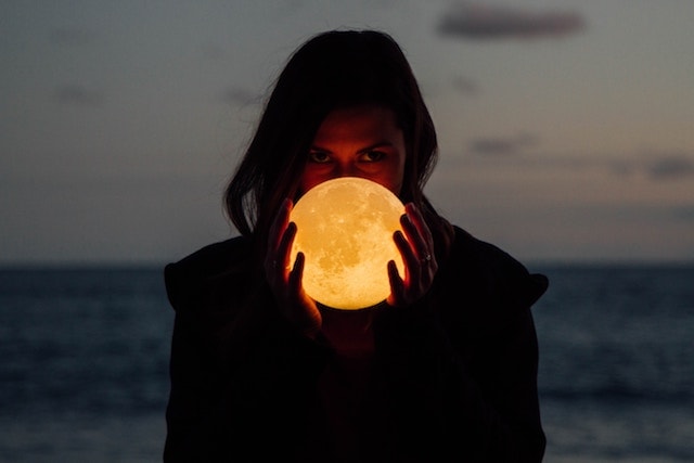 a woman holding a glowing yellow full moon. 